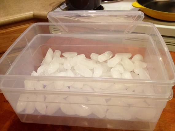 Two containers stacked, one  on top with holes drilled in and filled with ice.